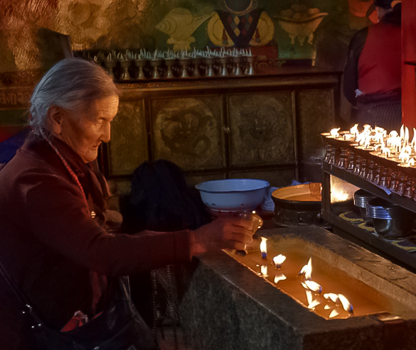 tibetan pilgrims add oil to yak butter lamp